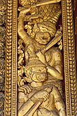 Wat Xieng Thong temple in Luang Prabang, Laos. Detail of a wooden door of the sim with gilded carvings on a red background. 